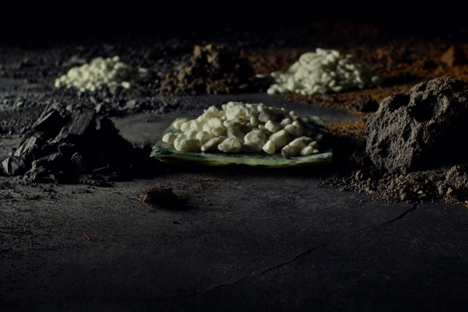Tas séparés de charbon horticole, de gravier clair et de roche volcanique sur une ardoise sombre
